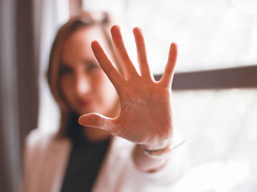 Close-up of a woman's hand gesturing stop with a blurred background indoors.