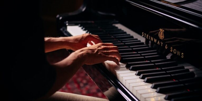 person playing black upright piano FEATURED IMAGE