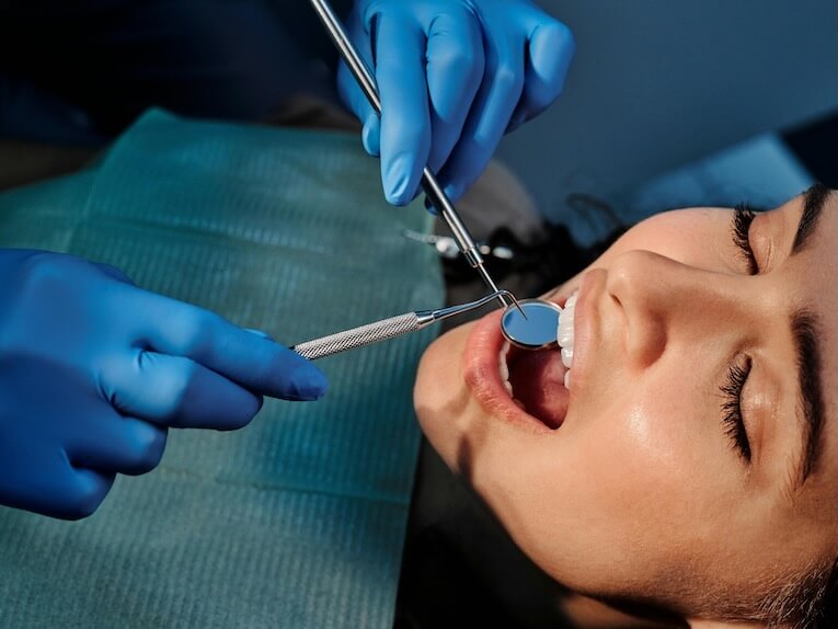 A Person Wearing Blue Latex Gloves Holding a Mirror in a Woman's Mouth
