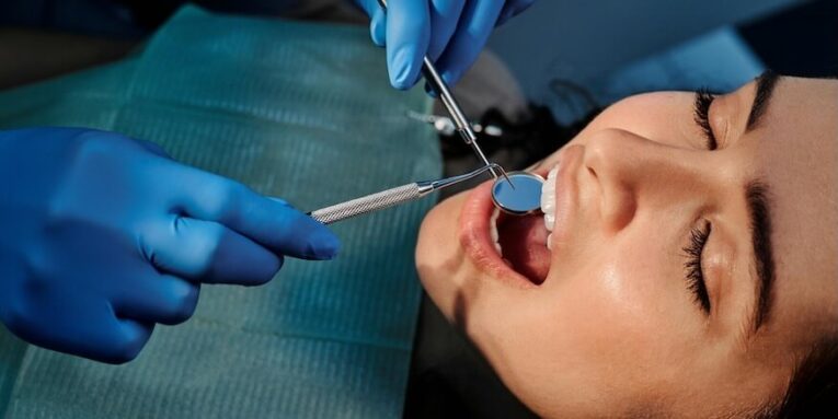 A Person Wearing Blue Latex Gloves Holding a Mirror in a Woman's Mouth FEATURED IMAGE