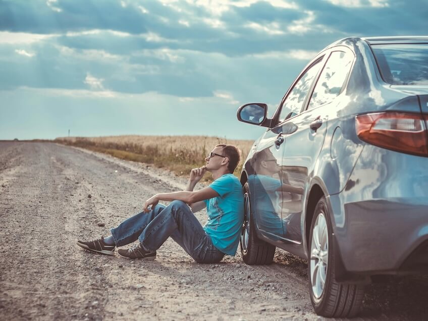 Contemplative Man Sitting by Roadside with Car