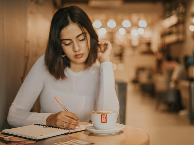 a woman sitting at a table writing in a notebook