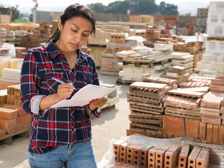 concentrated hispanic woman worker controlling quantity of bricks at hardware store warehouse