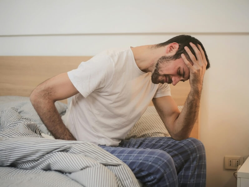 Young man in sleepwear suffering from headache in morning