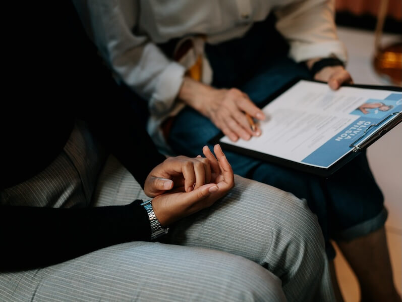 Person in White Long Sleeve Shirt Holding a Clipboard with Resume
