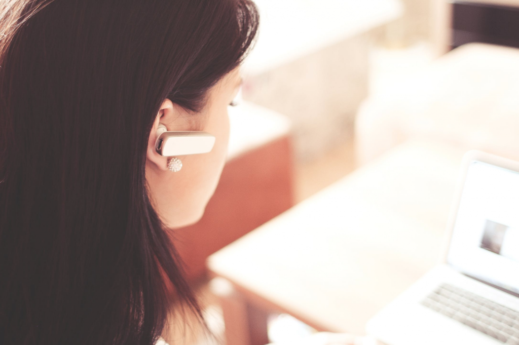 Woman Wearing Earpiece Using White Laptop Computer