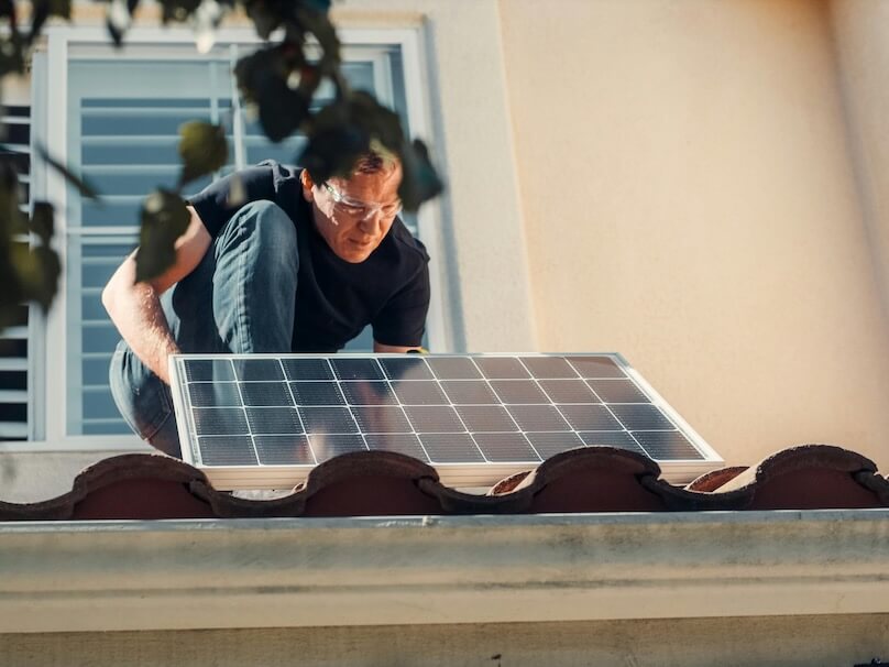 A Man in Black Shirt Installing a Solar Panel on the Roof