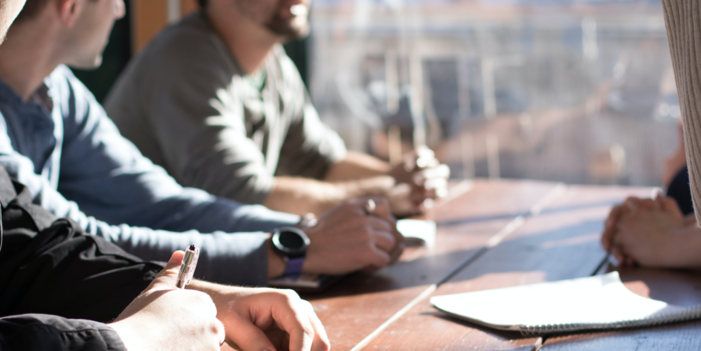 people sitting on chair in front of table while holding pens during daytime FEATURED IMAGE
