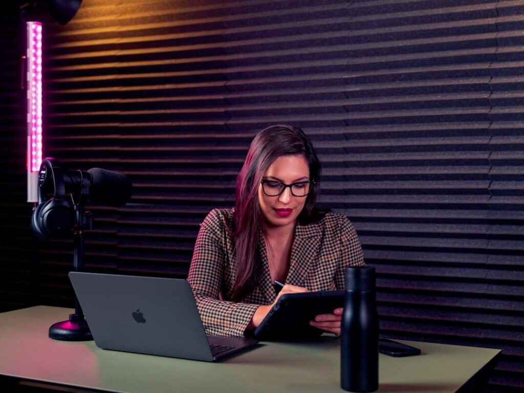 a woman sitting at a desk writing podcast content on a tablet 