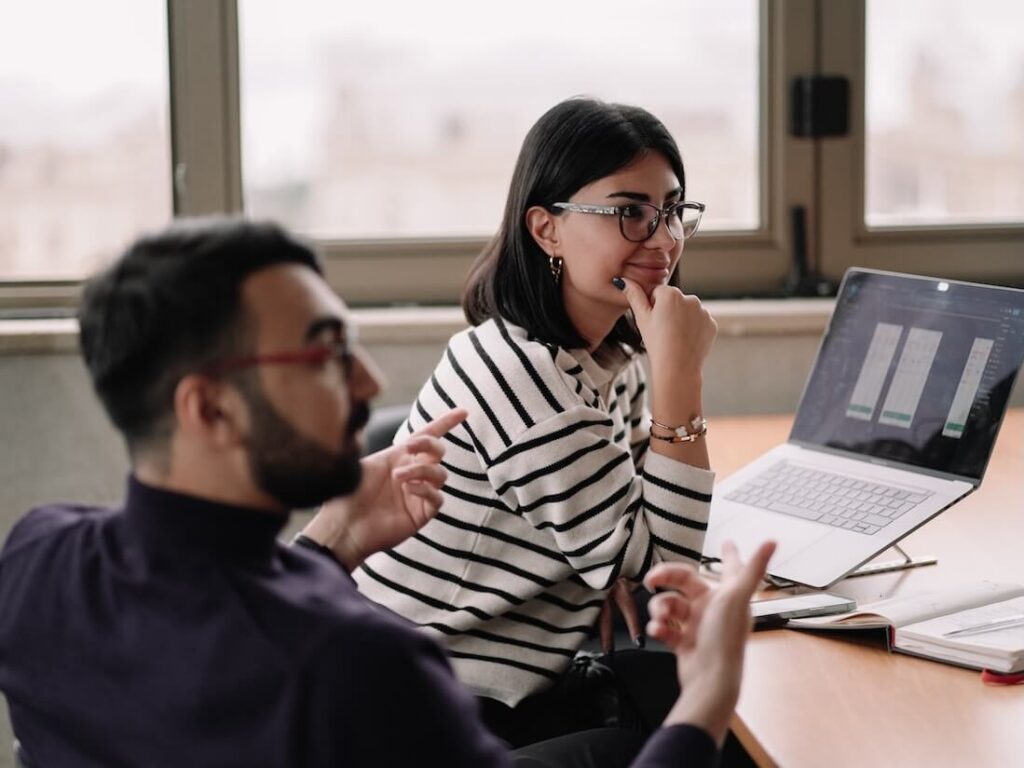 man and woman talking at a desk with laptop