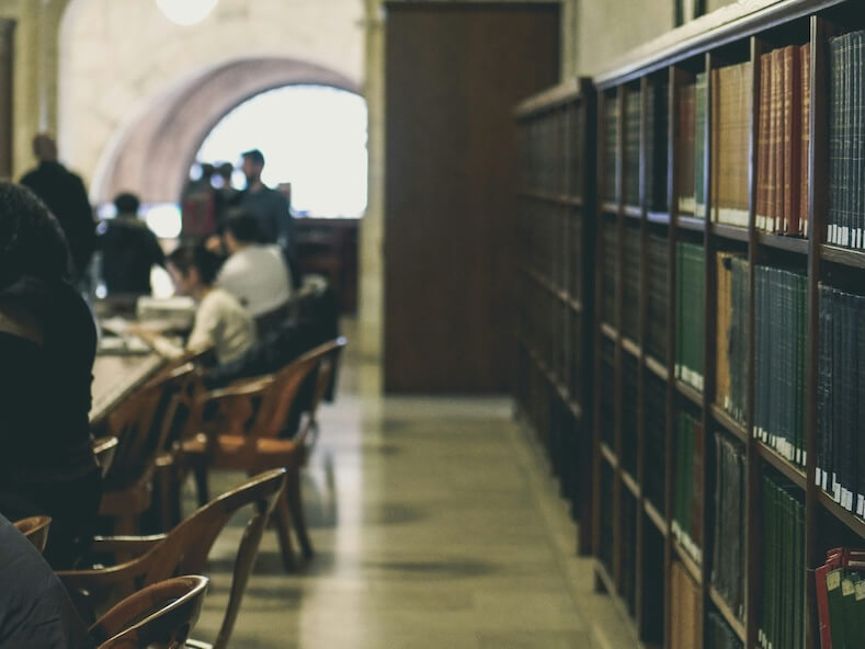 selective focus photography of books on bookcases near people sits in chairs