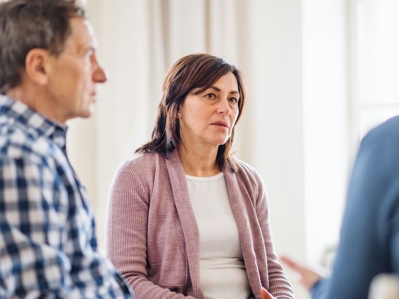 serious men and women sitting in a circle during group therapy talking
