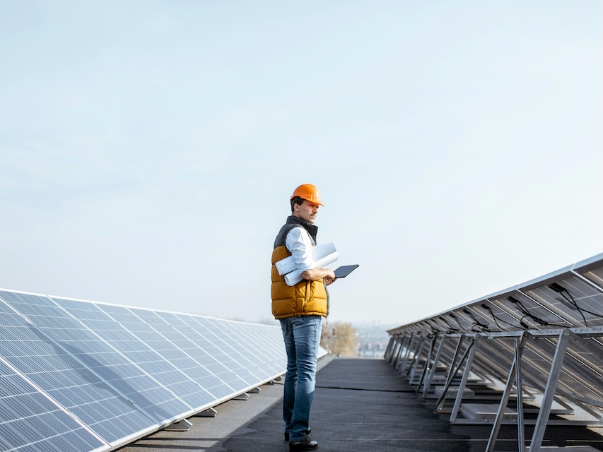 view on the rooftop solar power plant with man walking and examining photovoltaic panels concept of alternative energy and its service