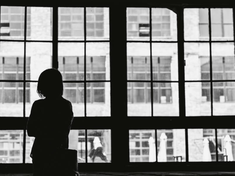 grayscale photography of depressed woman facing window