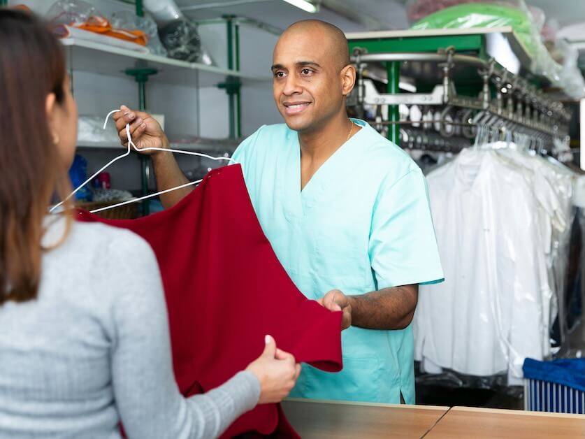 smiling man drycleaner giving clean garments to client satisfied with quality