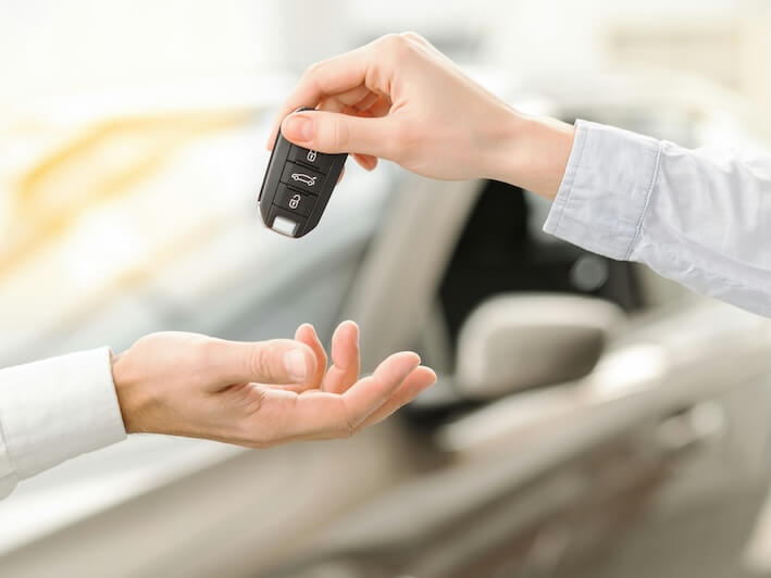 young man standing near the car getting keys rental service