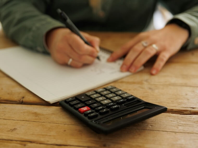 a person writing on a piece of paper next to a calculator
