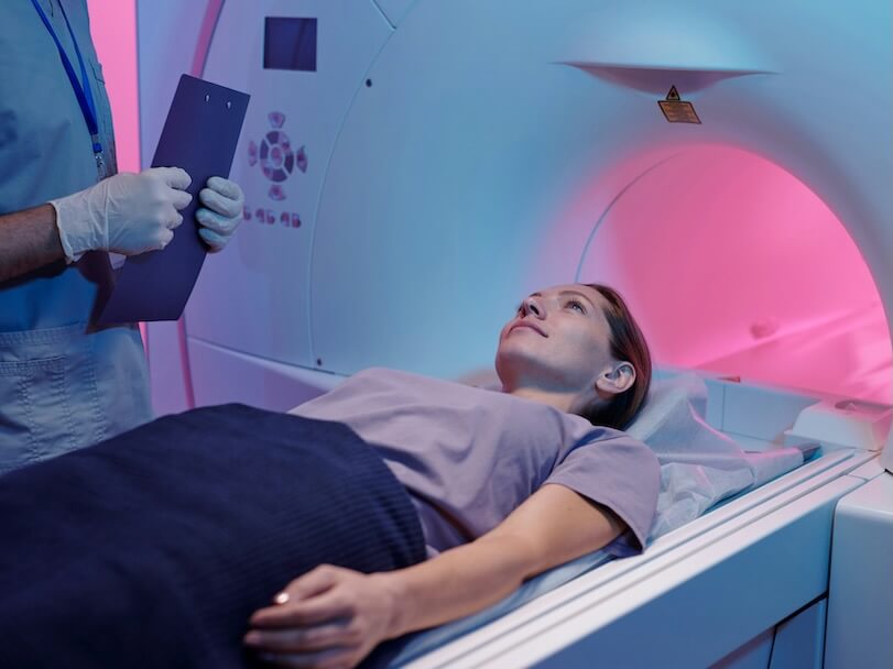 young female lying on long table of mri-scan machine while doctor standing by her