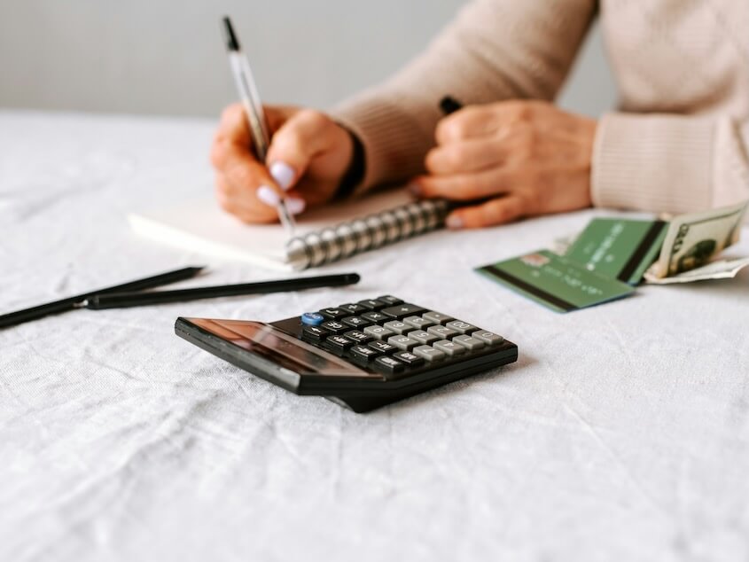 a person writing on a notepad next to a calculator