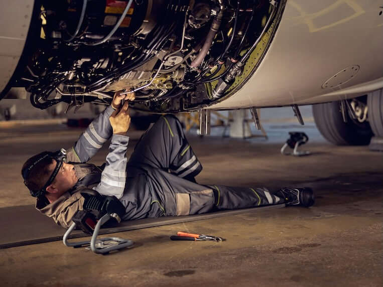 side view portrait of airplane maintenance mechanic inspecting on aircraft engine in aviation hangar