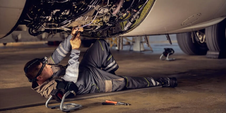 side view portrait of airplane maintenance mechanic inspecting on aircraft engine in aviation hangar FEATURED IMAGE