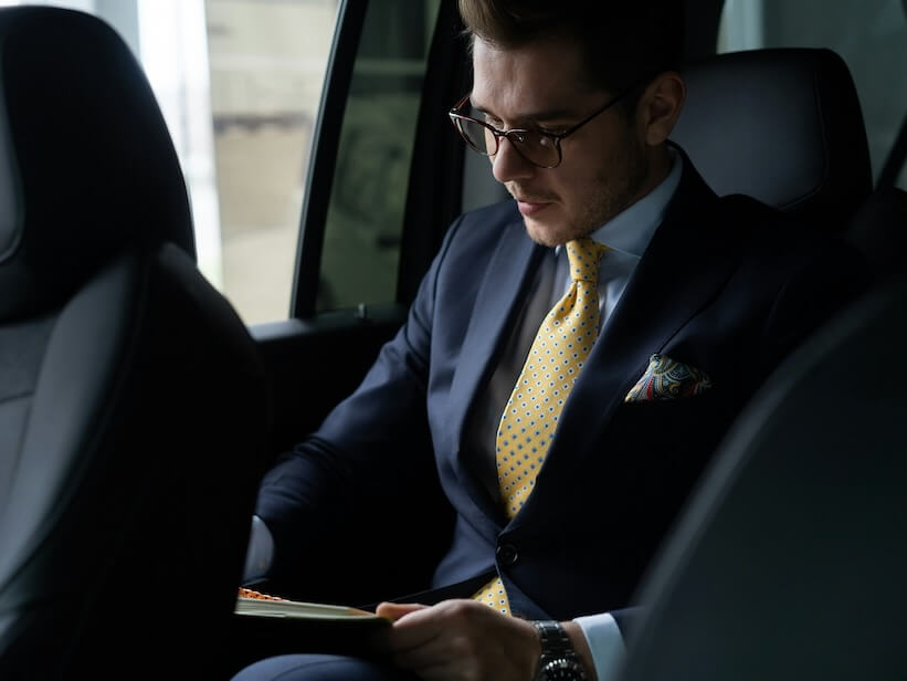 young businessman sitting on back seat of the car while his chauffeur is driving automobile