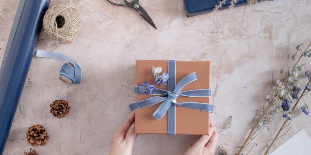 a person holding a wrapped gift box with a blue ribbon FEATURED IMAGE