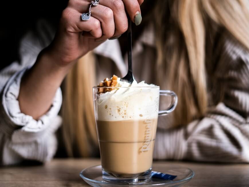 person holding clear glass mug with coffee and whip cream