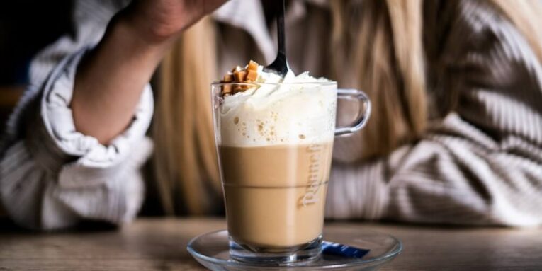 person holding clear glass mug with coffee and whip cream FEATURED IMAGE