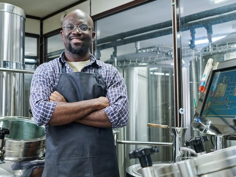 portrait of african american engineer smiling at camera standing with his arms crossed he working at modern brewery