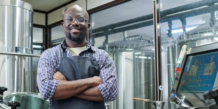 portrait of african american engineer smiling at camera standing with his arms crossed he working at modern brewery FEATURED IMAGE