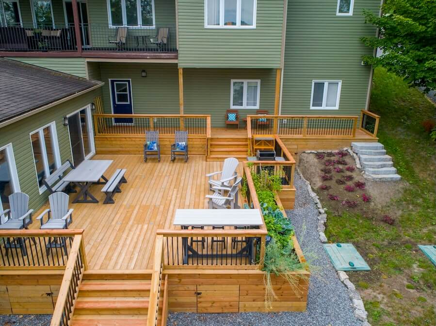 a deck with chairs and tables on it next to a house