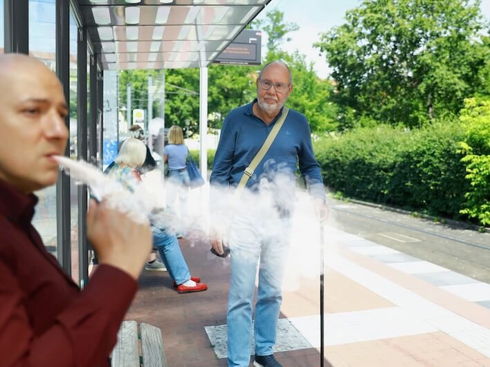 a man smoking a vape in front of a bus stop