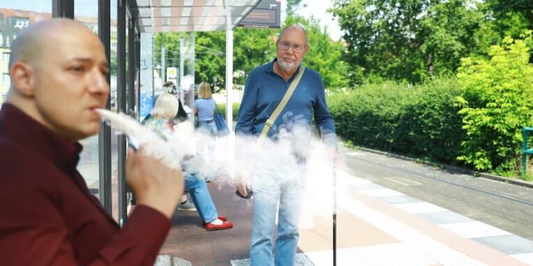 a man smoking a vape in front of a bus stop FEATURED IMAGE
