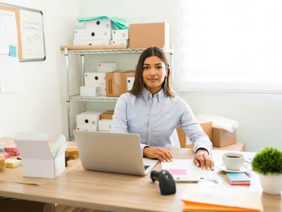 portrait of an hispanic young entrepreneur sitting at her office desk and working on making packages to ship to their customers