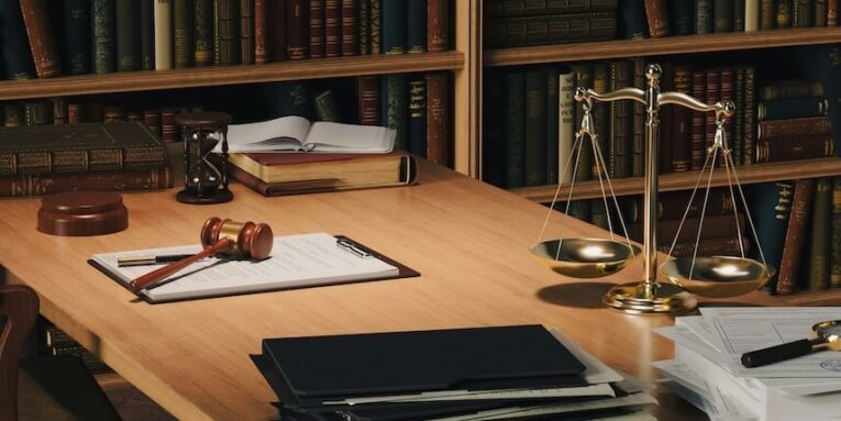a wooden desk topped with books and a judges scale FEATURED IMAGE