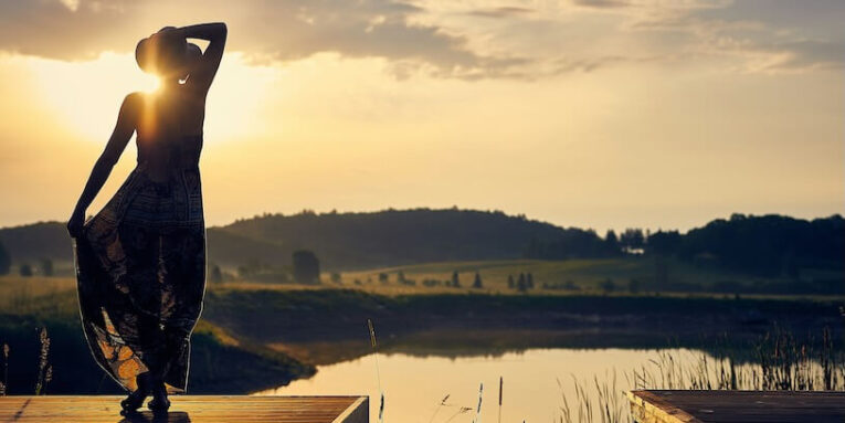 silhouette of woman standing on brown wooden dock during golden hour FEATURED IMAGE