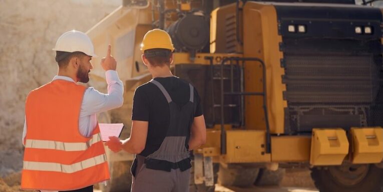 standing near haul truck and talking about document two men in uniform are working together in the quarry FEATURED IMAGE