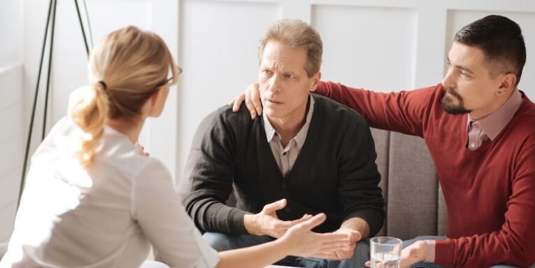 useful advice unhappy cheerless sad man looking at his therapist and listening to her while sitting with his boyfriend on the sofa FEATURED IMAGE