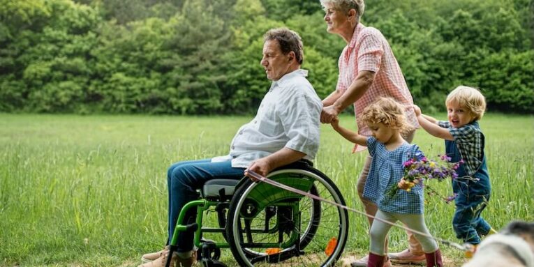 small children with senior grandparents in wheelchair and dog on a walk on meadow in nature FEATURED IMAGE