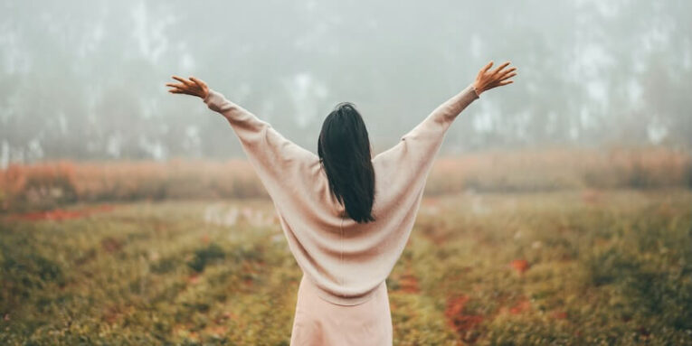 rear view of woman with open arms relaxing and enjoying the freedom in morning mist in forest FEATURED IMAGE