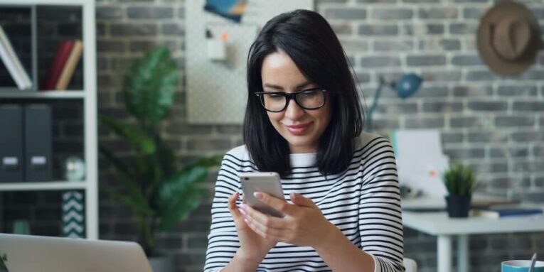 a woman sitting at a table looking at her cell phone FEATURED IMAGE