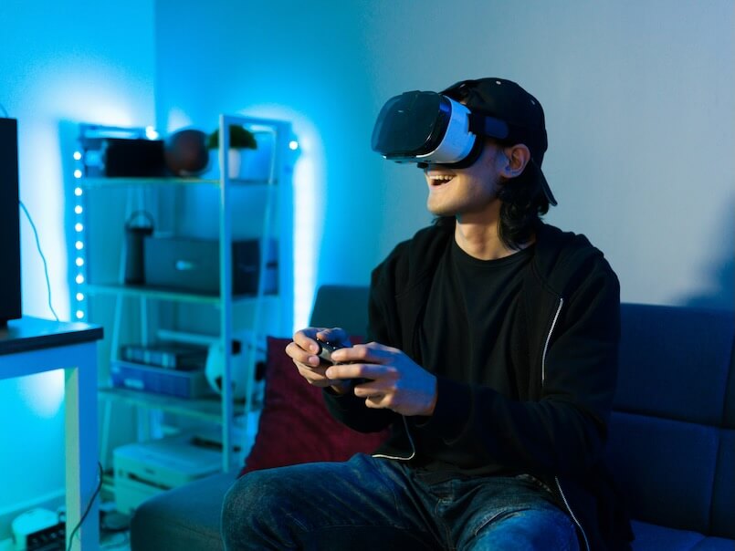 happy young man smiling and feeling excited while using virtual reality glasses and a remote controller to play a video game