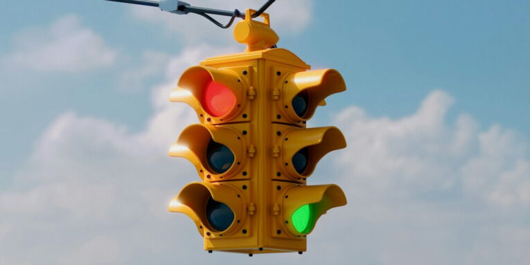 a traffic light hanging from a wire with a sky background FEATURED IMAGE