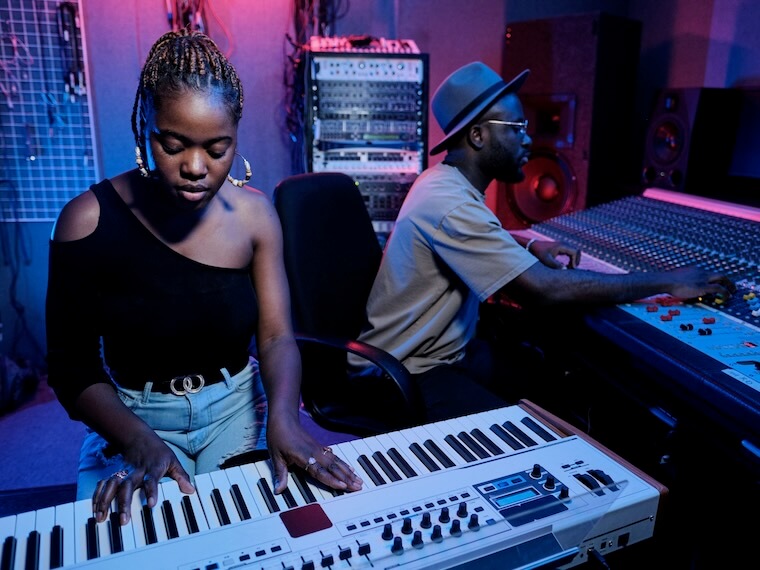 modern young african american female musician playing digital keyboard while sound engineer working on mixer in recording studio