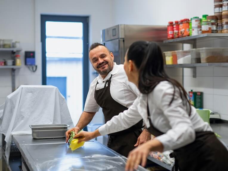 a chef and cook cleaning the workspace after doing dishes indoors in restaurant kitchen