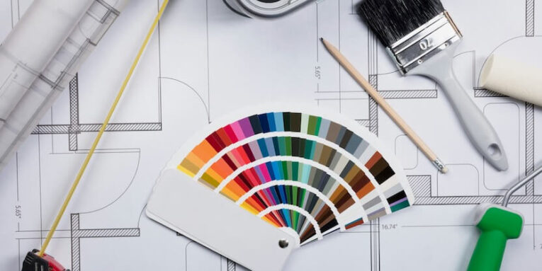 high angle view of color guide swatch on blueprints with paint roller and paint brush FEATURED IMAGE