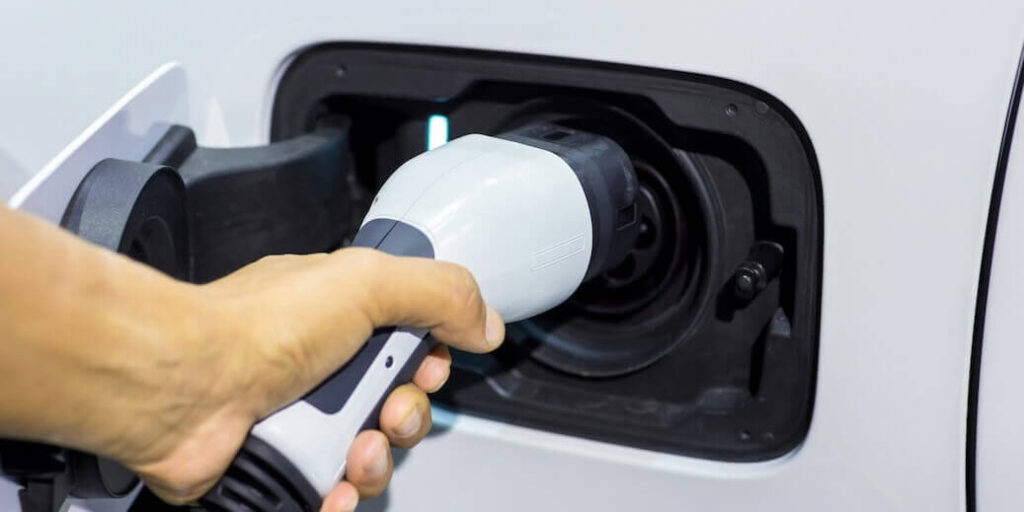 hand holding electric car charger electric vehicle ev-charging station and charger human hand is holding electric car charging connect to electric car FEATURED IMAGE