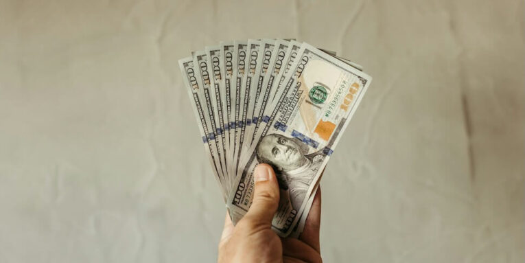 a hand holding a stack of twenty dollar bills FEATURED IMAGE