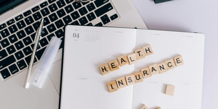 A Health Insurance Spelled on Scrabble Blocks on Top of a Notebook Planner FEATURED IMAGE